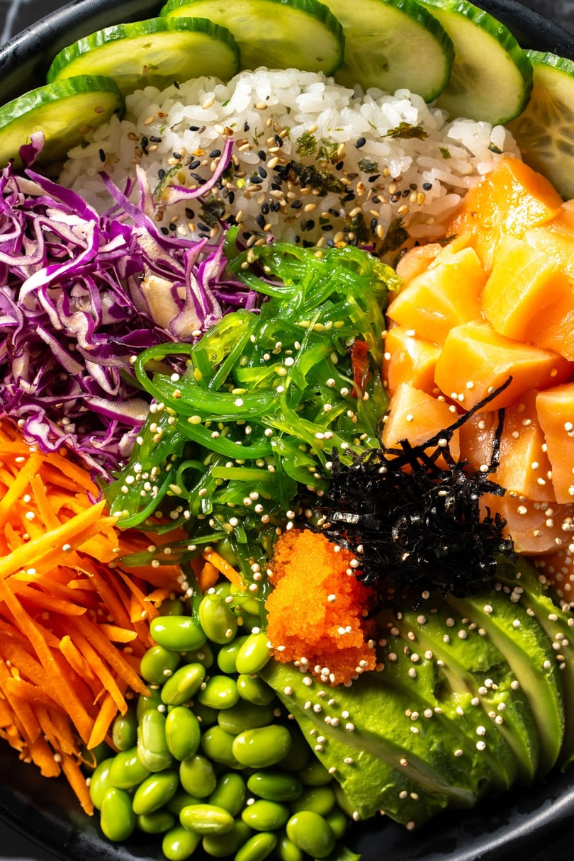 Close-up of a colorful poke bowl with salmon, avocado, edamame, seaweed, and various toppings.