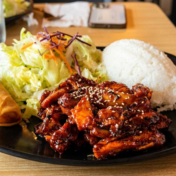 Teriyaki chicken with white rice, a side salad, and an egg roll on a black plate.