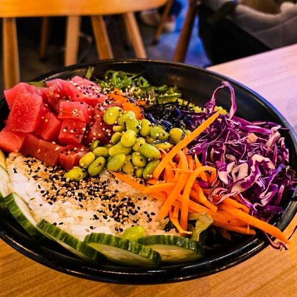 Colorful poke bowl with tuna, edamame, carrots, purple cabbage, and cucumber on a wooden table.