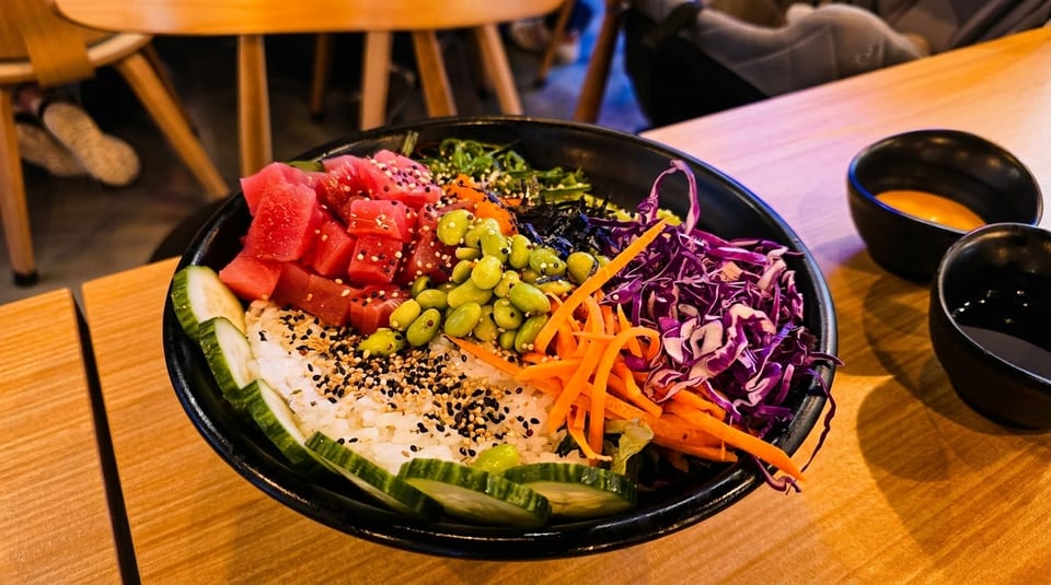 Colorful poke bowl with tuna, edamame, carrots, purple cabbage, and cucumber on a wooden table.