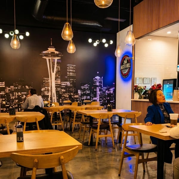 Restaurant interior with a Seattle skyline mural, wooden tables, and people dining.