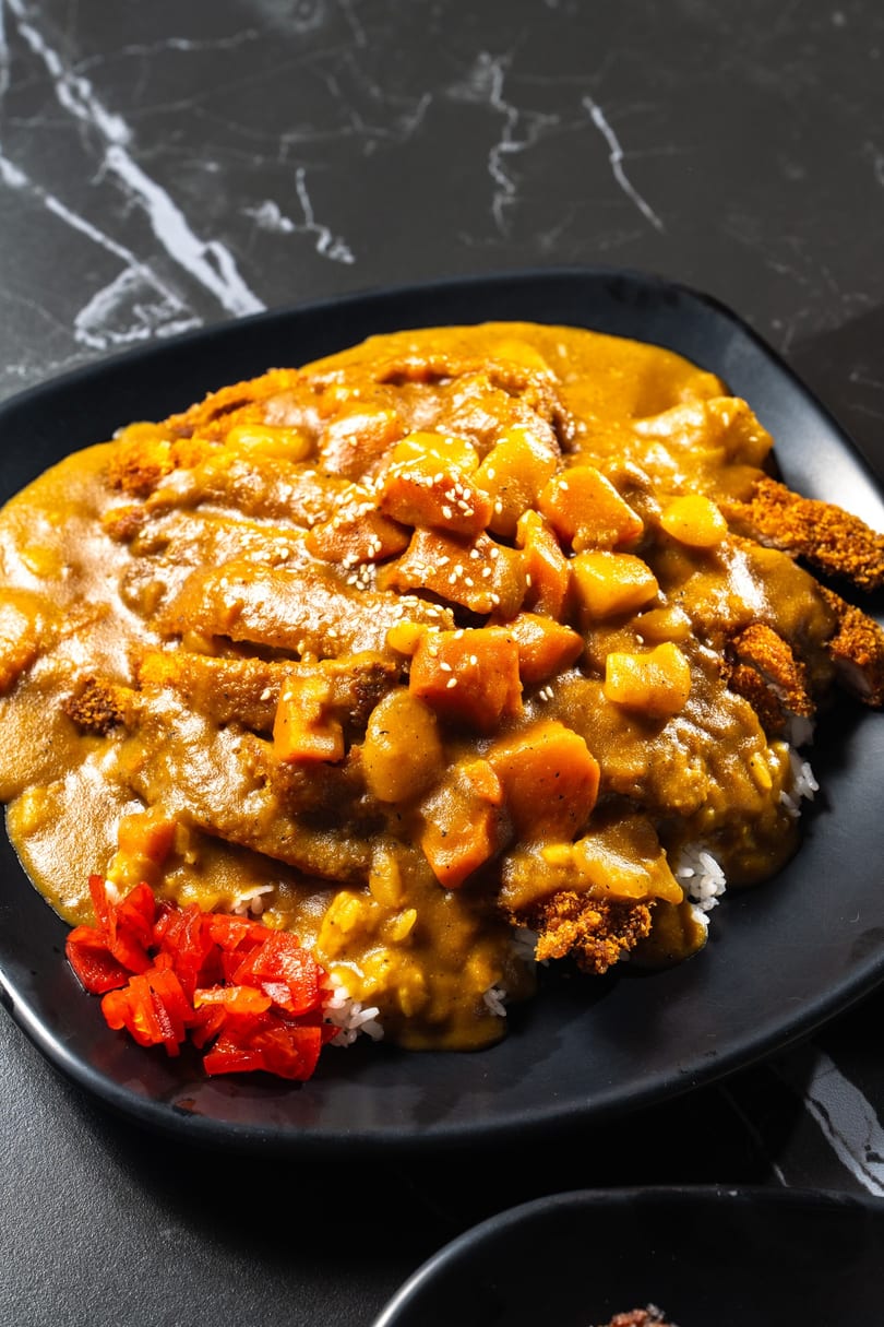 Japanese chicken katsu curry with rice, potatoes, carrots, sesame seeds, and red pickles.
