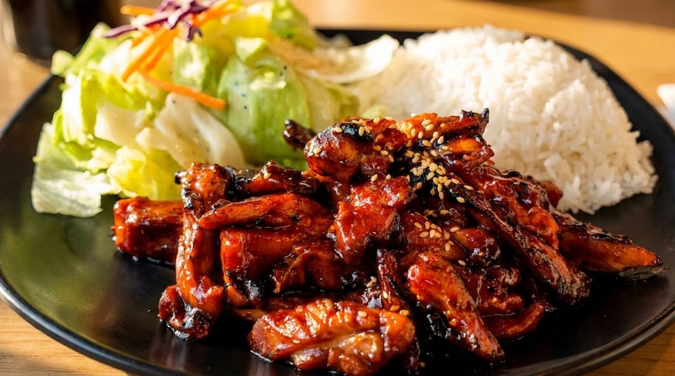 Teriyaki chicken with sesame seeds, white rice, and a side salad on a black plate.