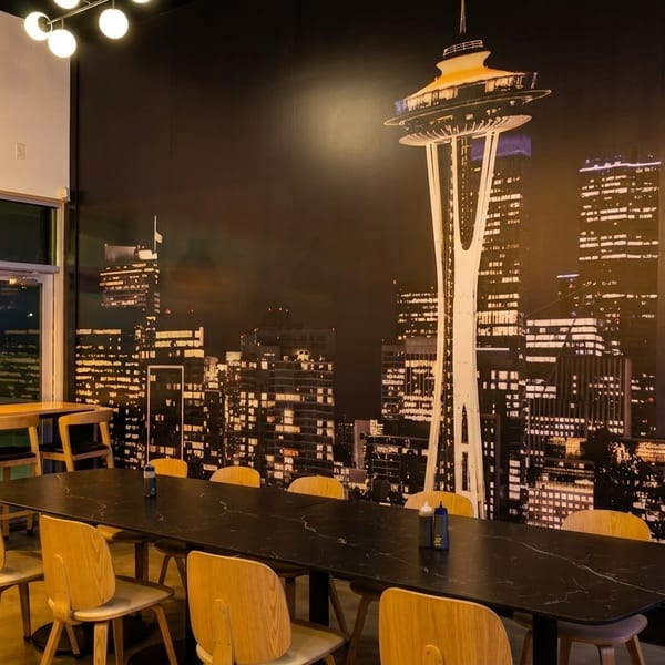 Restaurant interior with a long table, bar seating, and a large mural of the Seattle skyline.